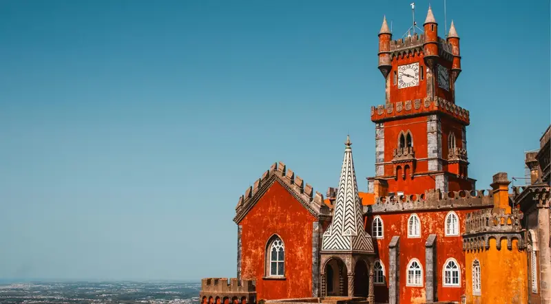 The red clock tower of Pena Palace against a clear blue sky in Sintra